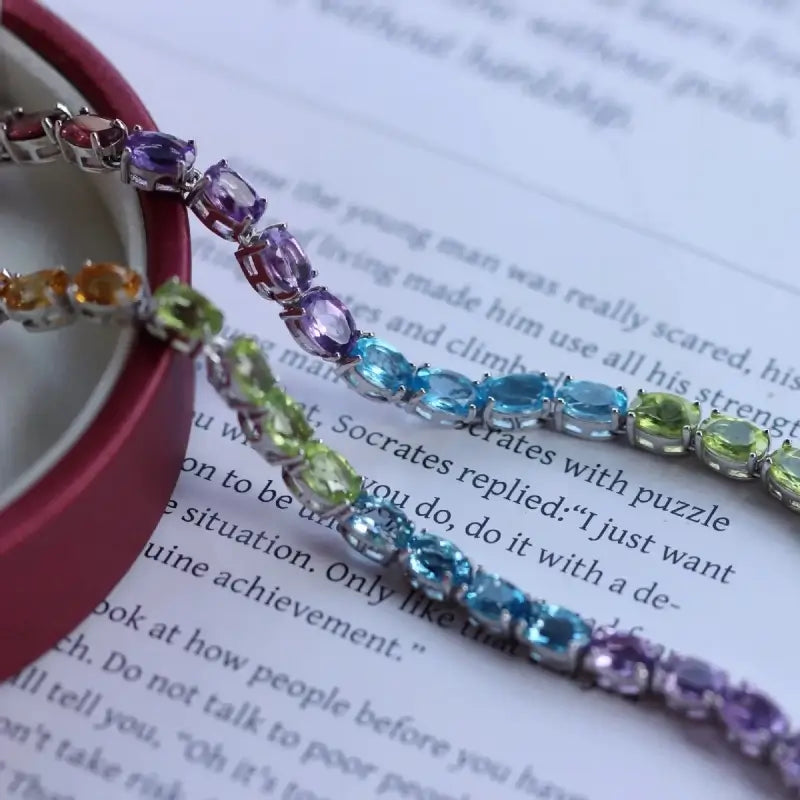 Sterling Silver Natural Crystals Rainbow Tennis Bracelet by Sheehas. The bracelet is made of 925 sterling silver plated with 18K white gold, and is composed of oval-cut garnet, amethyst, topaz, peridot, and citrine arranged in sequence. The bracelet is adjustable in length, suitable for wrists with a circumference of 15cm to 20cm.