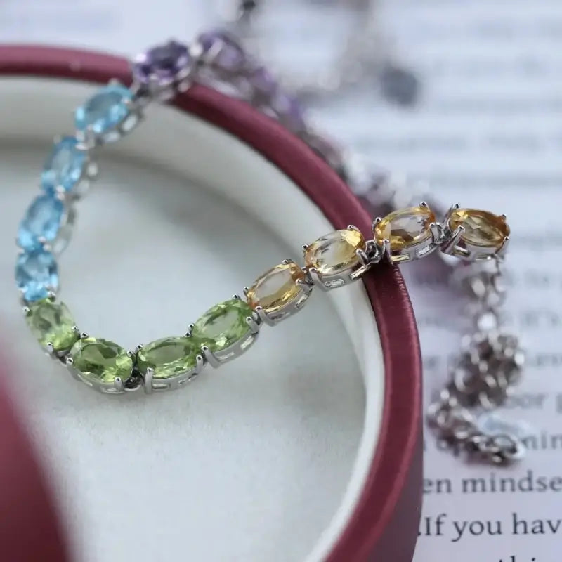 Sterling Silver Natural Crystals Rainbow Tennis Bracelet by Sheehas. The bracelet is made of 925 sterling silver plated with 18K white gold, and is composed of oval-cut garnet, amethyst, topaz, peridot, and citrine arranged in sequence. The bracelet is adjustable in length, suitable for wrists with a circumference of 15cm to 20cm.