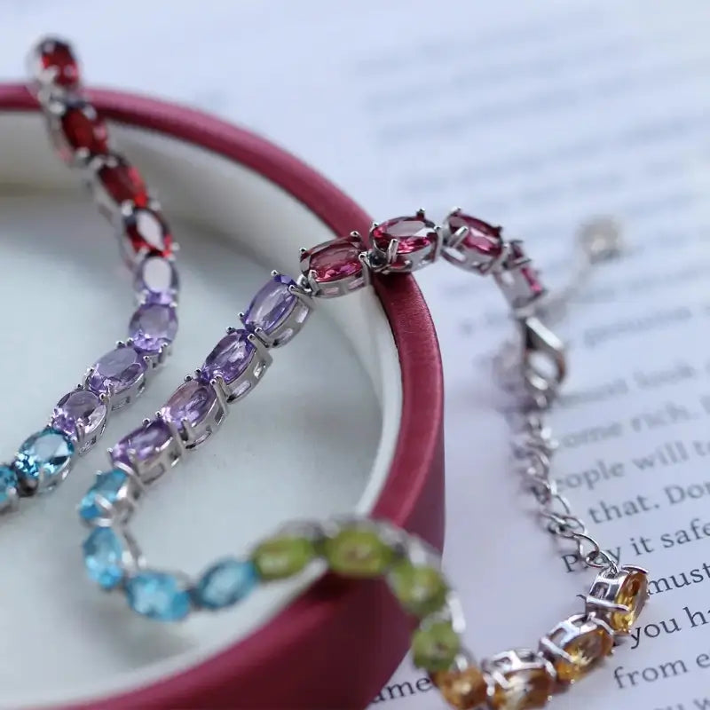Sterling Silver Natural Crystals Rainbow Tennis Bracelet by Sheehas. The bracelet is made of 925 sterling silver plated with 18K white gold, and is composed of oval-cut garnet, amethyst, topaz, peridot, and citrine arranged in sequence. The bracelet is adjustable in length, suitable for wrists with a circumference of 15cm to 20cm.