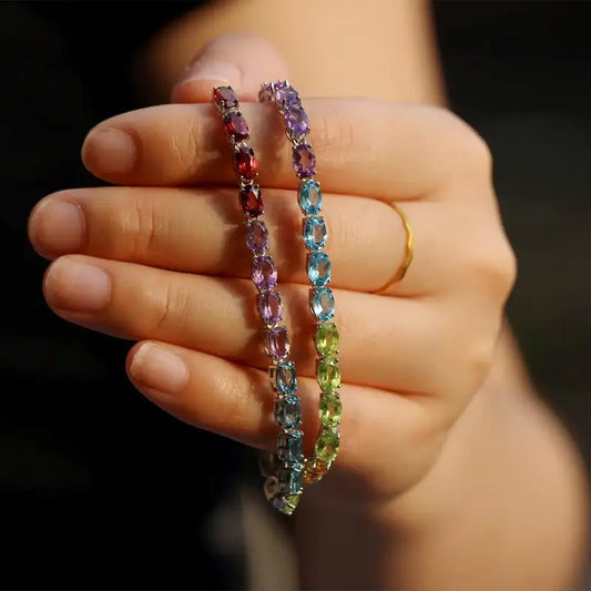 Sterling Silver Natural Crystals Rainbow Tennis Bracelet by Sheehas. The bracelet is made of 925 sterling silver plated with 18K white gold, and is composed of oval-cut garnet, amethyst, topaz, peridot, and citrine arranged in sequence. The bracelet is adjustable in length, suitable for wrists with a circumference of 15cm to 20cm.
