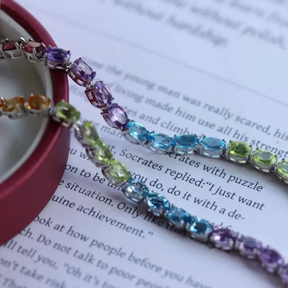 Sterling Silver Natural Crystals Rainbow Tennis Bracelet by Sheehas. The bracelet is made of 925 sterling silver plated with 18K white gold, and is composed of oval-cut garnet, amethyst, topaz, peridot, and citrine arranged in sequence. The bracelet is adjustable in length, suitable for wrists with a circumference of 15cm to 20cm.