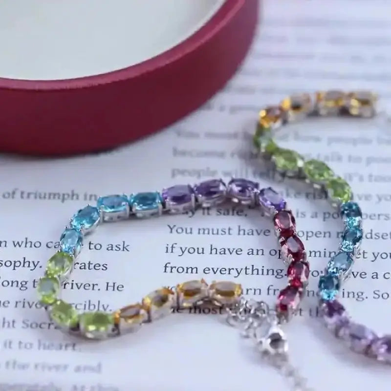 Sterling Silver Natural Crystals Rainbow Tennis Bracelet by Sheehas. The bracelet is made of 925 sterling silver plated with 18K white gold, and is composed of oval-cut garnet, amethyst, topaz, peridot, and citrine arranged in sequence. The bracelet is adjustable in length, suitable for wrists with a circumference of 15cm to 20cm.