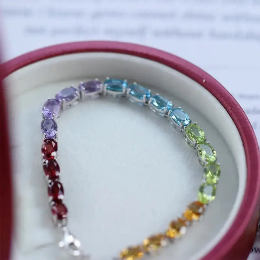 Sterling Silver Natural Crystals Rainbow Tennis Bracelet by Sheehas. The bracelet is made of 925 sterling silver plated with 18K white gold, and is composed of oval-cut garnet, amethyst, topaz, peridot, and citrine arranged in sequence. The bracelet is adjustable in length, suitable for wrists with a circumference of 15cm to 20cm.